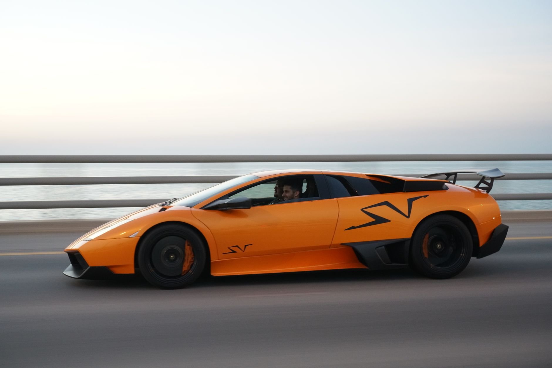 A luxury sports car driving on a coastal highway at sunset